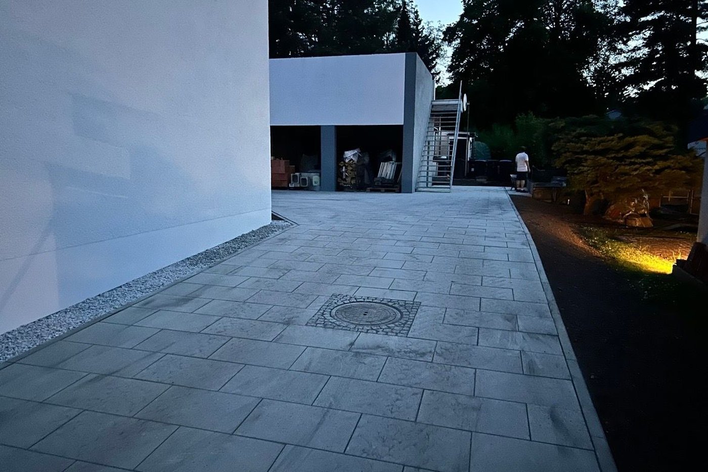 Fertige Hoffläche aus großformatigen Platten mit Schachtabdeckung in der Dämmerung