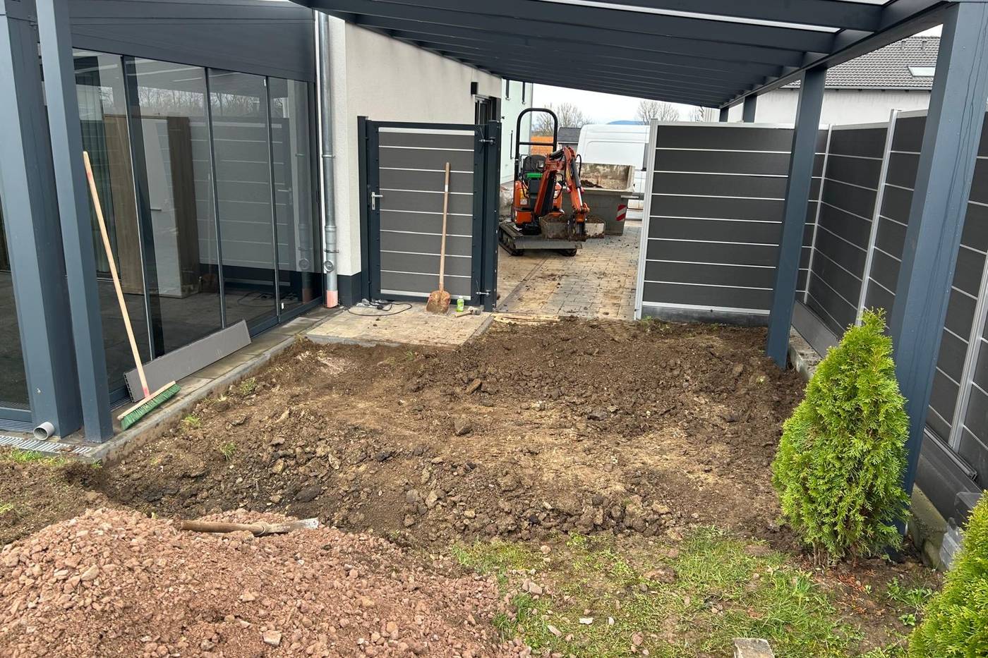 Minibagger hebt die Fläche unter einem Carport aus — Arbeiten auf engem Raum