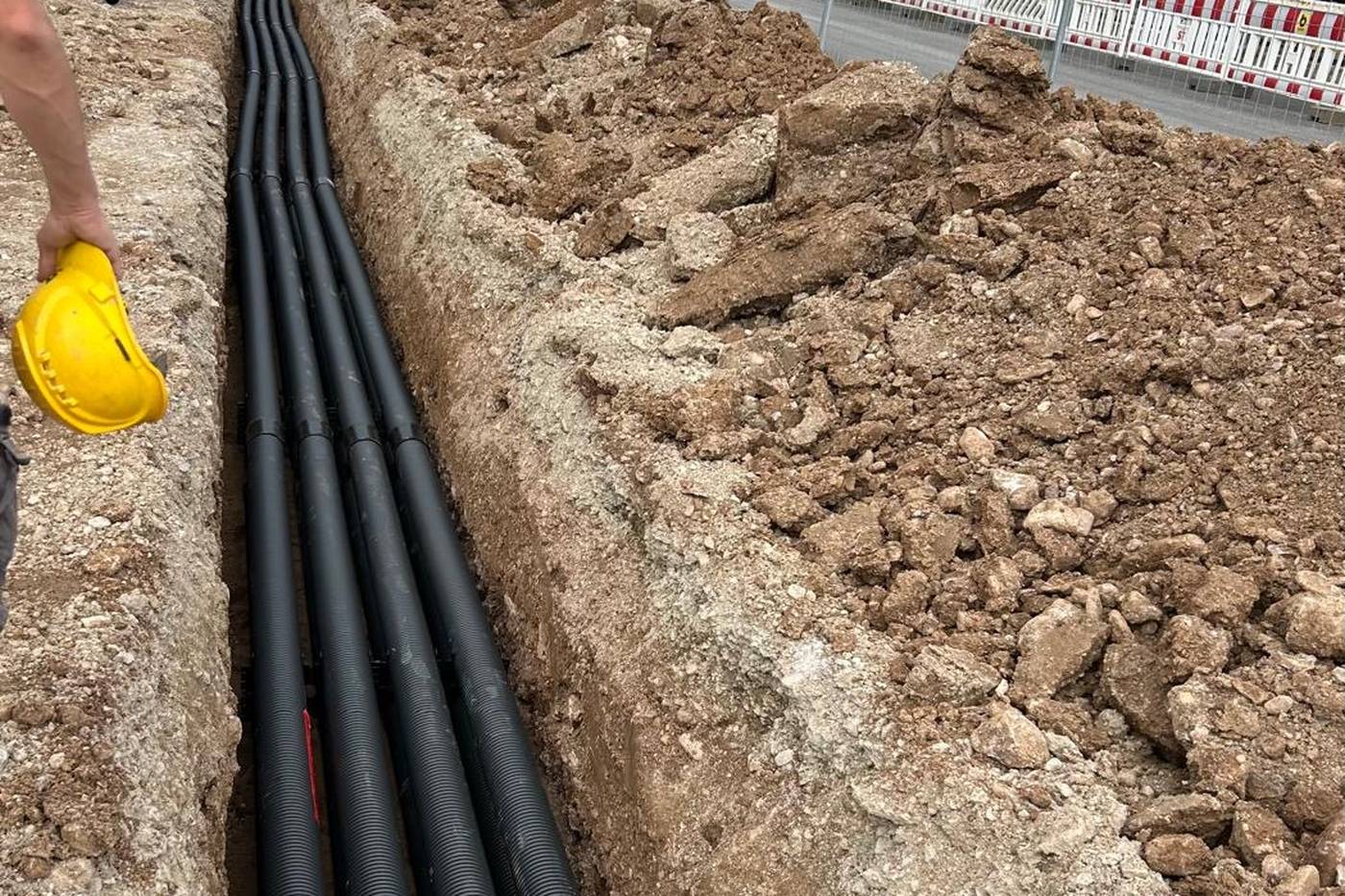 Offener Leitungsgraben an einer Straße, Leerrohre in der Sohle, Bauzaun am Rand