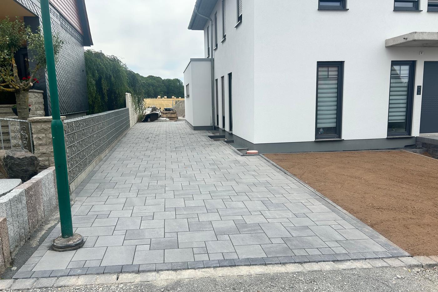 Fertig gepflasterte Zufahrt zwischen zwei Wohnhäusern mit Betonsteinpflaster und Randeinfassung