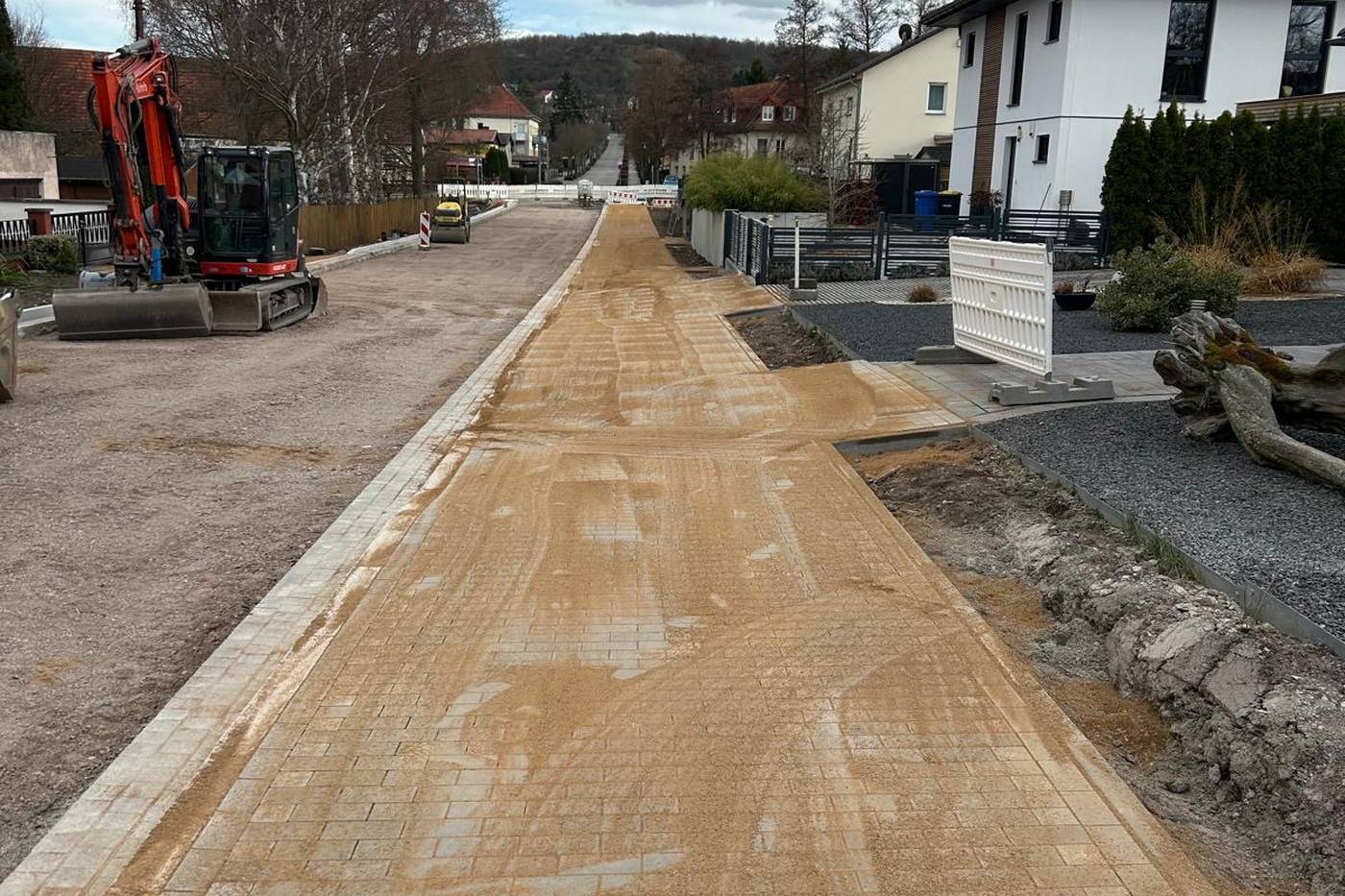 Frisch gepflasterte Straße mit eingefegtem Sand, Bagger und gesetzter Randeinfassung